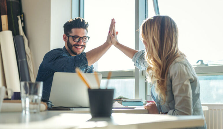 Zwei Personen an einem Tisch klatschen sich mit den Händen ab. High Five.