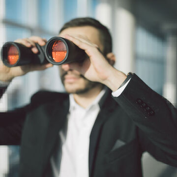 Ein Mann im Anzug schaut durch ein Fernglas.