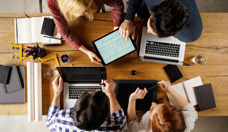Personen mit Laptops sitzen am Tisch und besprechen sich.