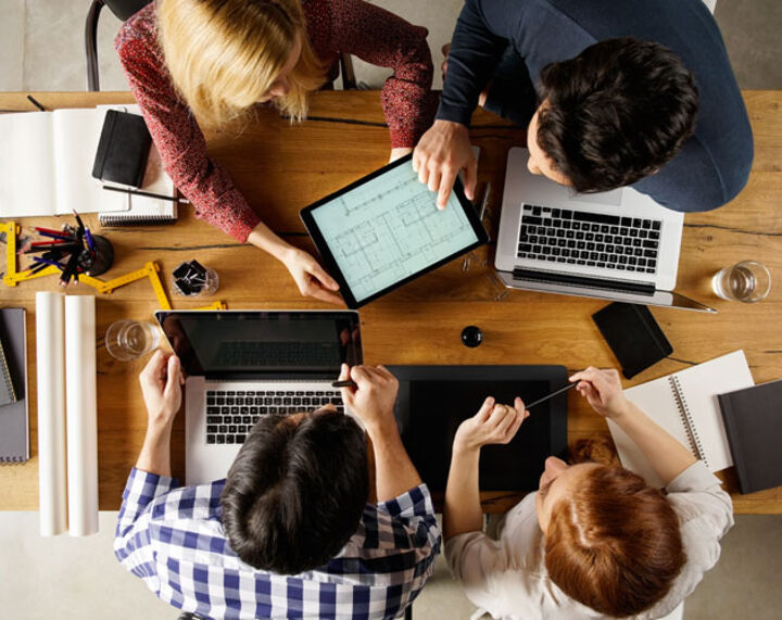 Personen mit Laptops sitzen am Tisch und besprechen sich.