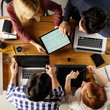 Personen mit Laptops sitzen am Tisch und besprechen sich.