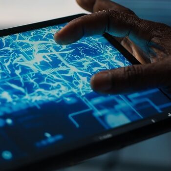 Eine Person bedient ein Tablet, auf dessen Bildschirm ein digitales Gehirn mit leuchtenden neuronalen Verbindungen dargestellt ist. Das Motiv symbolisiert Künstliche Intelligenz, maschinelles Lernen und die Verarbeitung komplexer Daten in einer vernetzten, digitalen Umgebung.