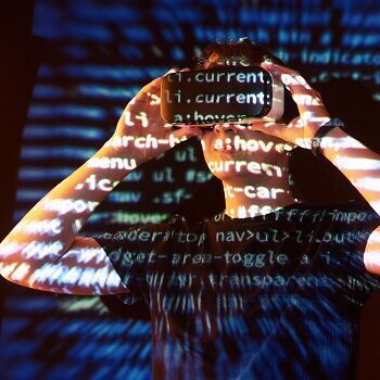 Mann steht mit einer VR-Brille auf dem Kopf vor einer wand welche durch einen Beamer mit code bestrahlt wird 