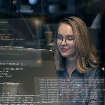 HTML- und CSS-Collage schweben vor einer Frau welche an einem Tisch vor einem Monitor sitzt.