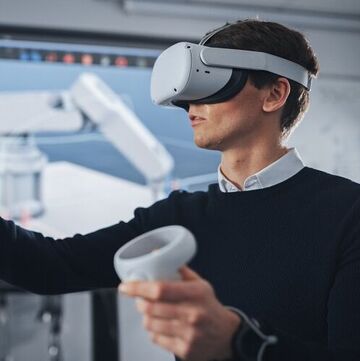 Ingenieurstudent mit Virtual-Reality-Headset, der Joysticks hält und bionische Gliedmaßen steuert, während die Aktionen auf dem Bildschirm angezeigt werden. Moderne Ausrüstung und Informatikausbildung im Universitätskonzept.