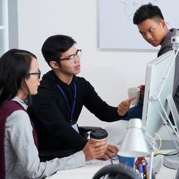 Drei Menschen sitzen an einem Schreibtisch vor einem Computer und diskutieren.