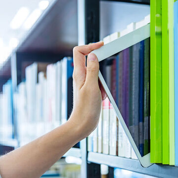 Eine Person stellt ein Tablet in ein Bücherregal oder nimmt es heraus.