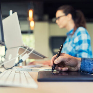 Personen arbeiten am PC mit einem Zeichenpad.