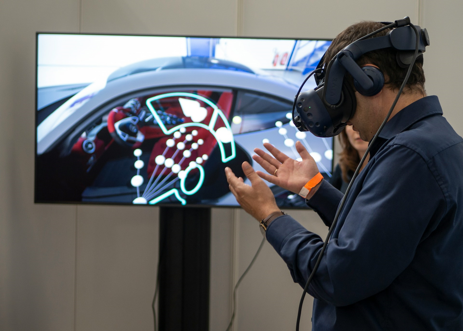 Mann mit Virtual-Reality-Headset im Hintergrund ist ein Digitales Auto zu sehen