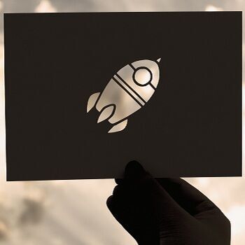 Hand hält einen karton auschnitt einer Rakete gegen bewölkten Himmel