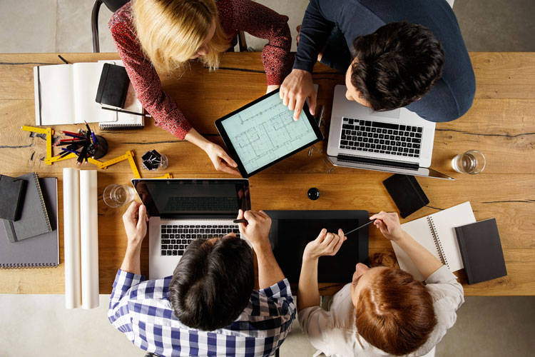 Personen mit Laptops sitzen am Tisch und besprechen sich.