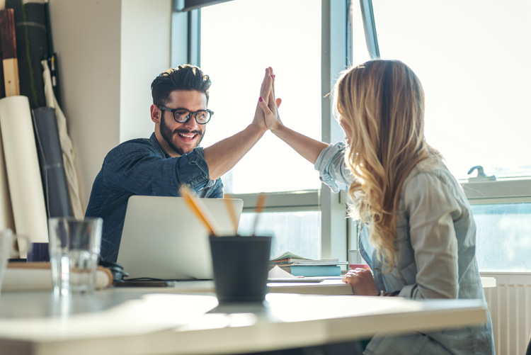 Zwei Personen an einem Tisch klatschen sich mit den Händen ab. High Five.