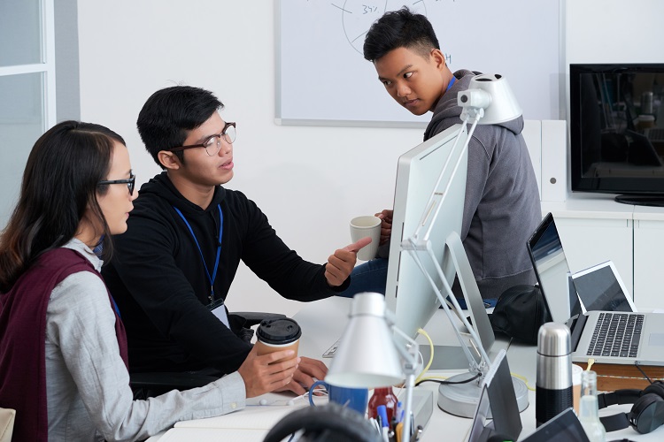 Drei Menschen sitzen an einem Schreibtisch vor einem Computer und diskutieren.