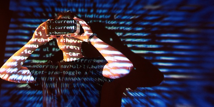 Mann steht mit einer VR-Brille auf dem Kopf vor einer wand welche durch einen Beamer mit code bestrahlt wird 