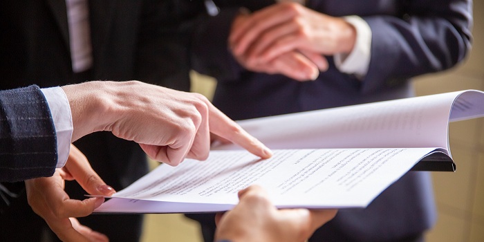 Mehrere Personen in Anzügen stehen zusammen und betrachten ein Dokument. Eine Person zeigt mit dem Finger auf eine Textstelle, während eine andere das Papier hält