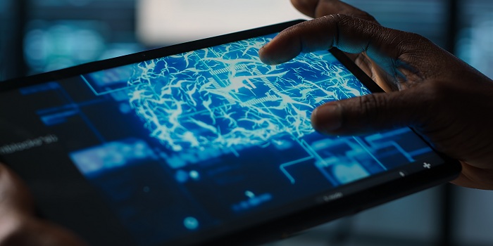 Eine Person bedient ein Tablet, auf dessen Bildschirm ein digitales Gehirn mit leuchtenden neuronalen Verbindungen dargestellt ist. Das Motiv symbolisiert Künstliche Intelligenz, maschinelles Lernen und die Verarbeitung komplexer Daten in einer vernetzten, digitalen Umgebung.