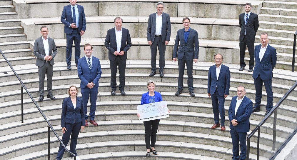 12 Personen stehen auf einer Treppe. Eine Person hat ein Check in der Hand